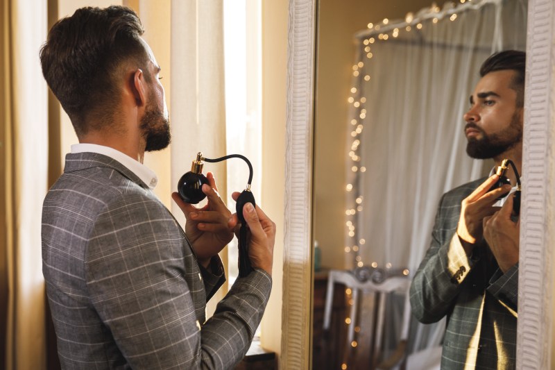 Young and handsome bearded man is using atomizer nozzle with perfume