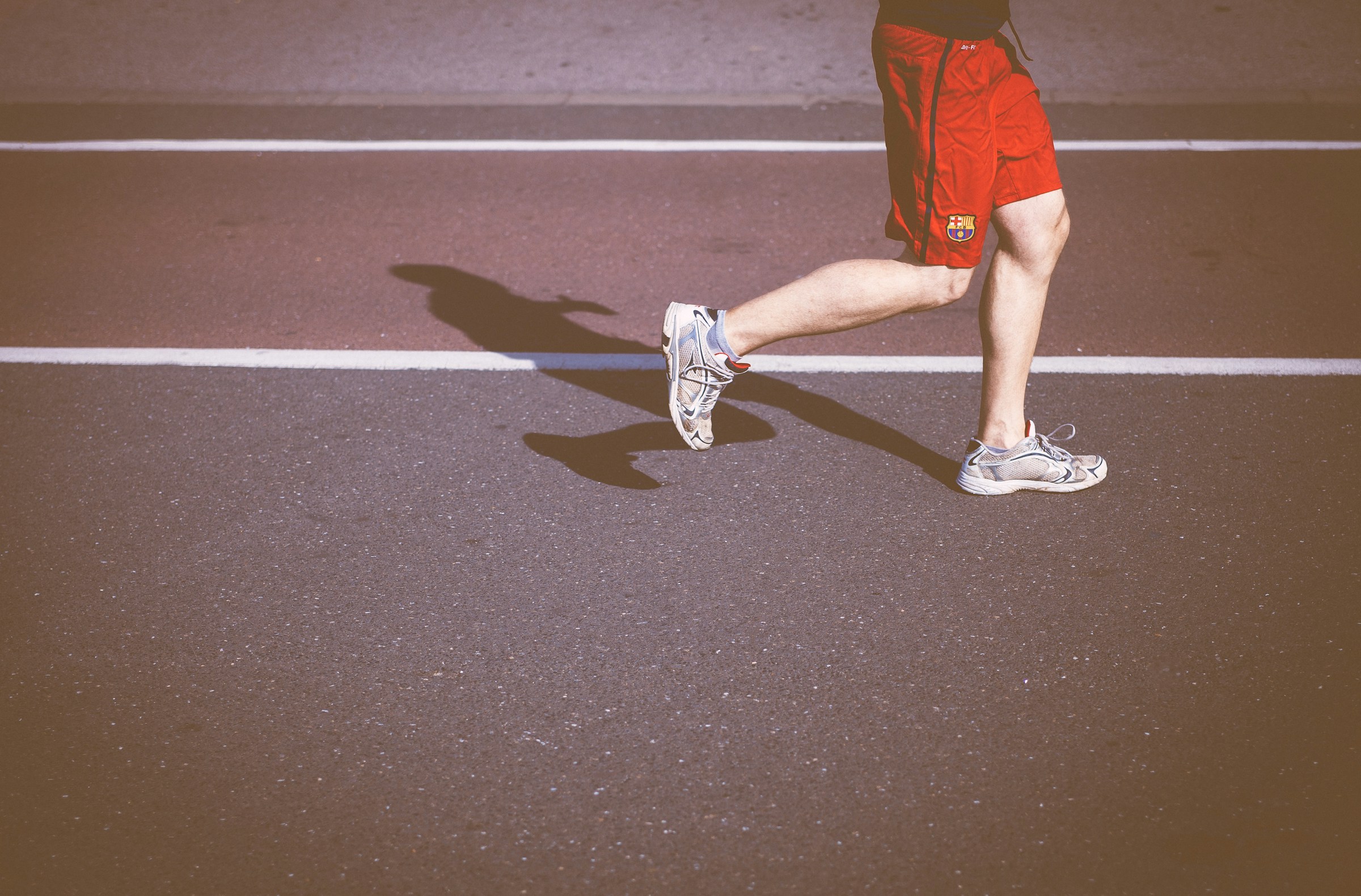 Man with red shorts legs running on track with shadow behind him