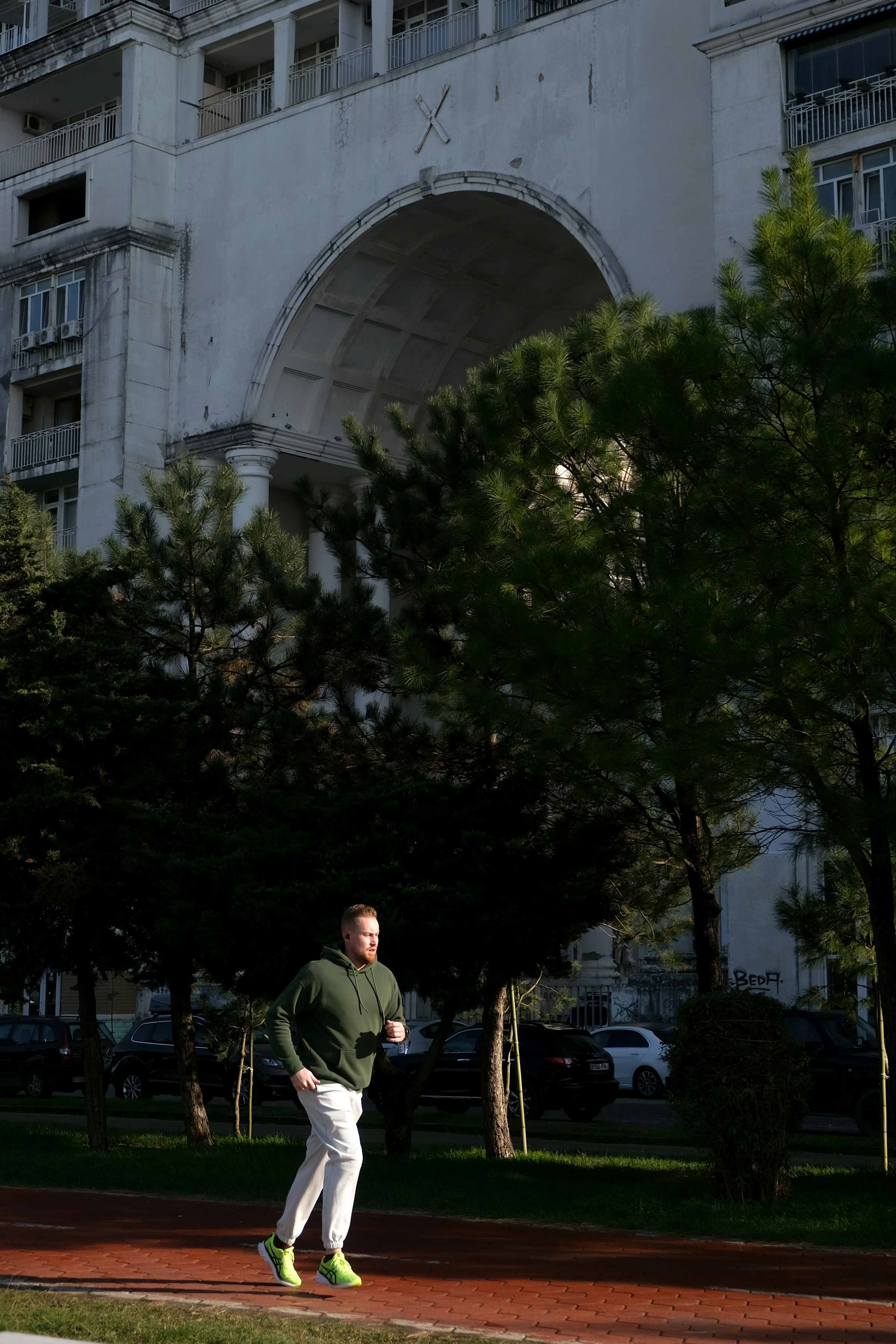 man in green hoodie running by building and trees