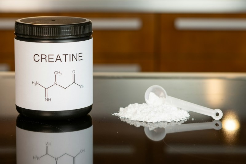 Creatine powder with some on table with a spoon